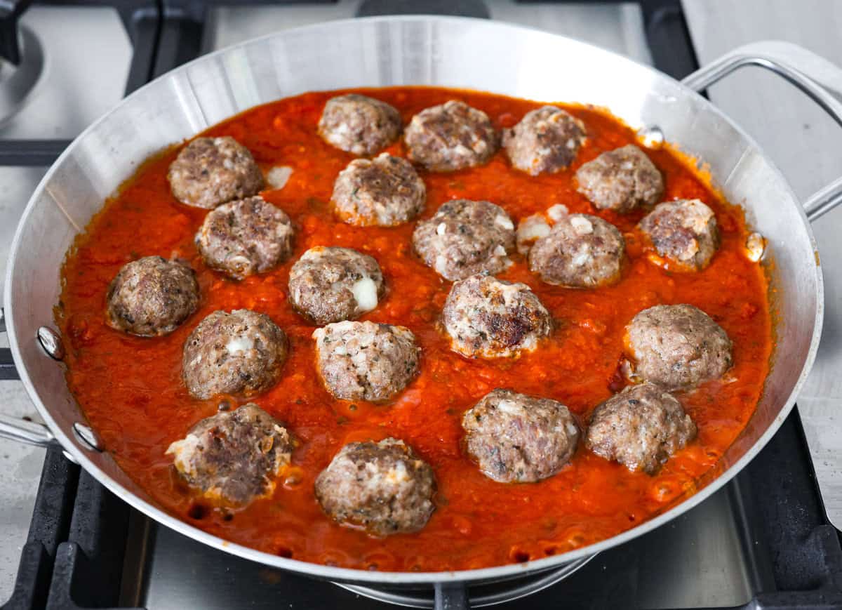 Mozzarella Stuffed Meatballs take classic meatballs to the next level! Tender and juicy with melty cheese on the inside. Serve these meatballs as a party appetizer or over spaghetti noodles for a hearty meal! Sixth photo of the mozzarella stuffed meatballs placed in a pan of marinara sauce.