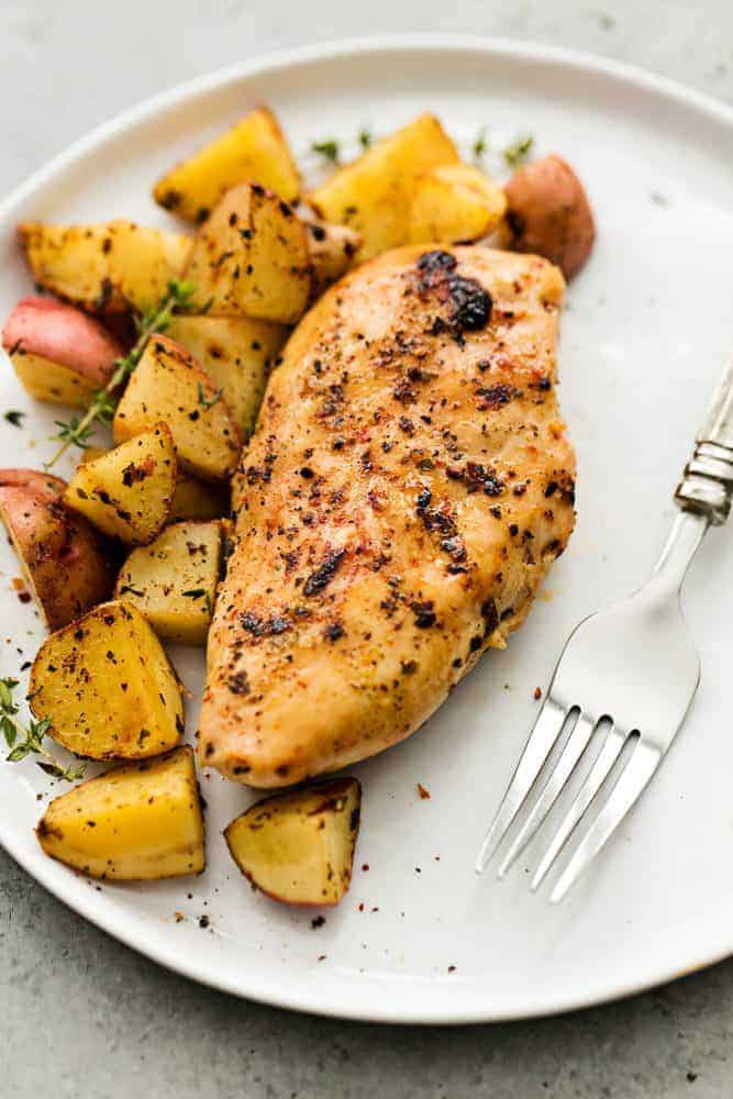 Slow cooker Italian chicken and potatoes on a white plate with a fork on the side.