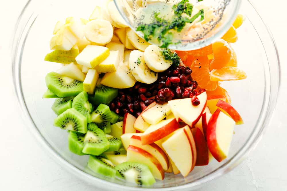 Ensalada de frutas de invierno con plátanos, manzanas, naranjas, kiwi y granadas con aderezo de semillas de amapola.