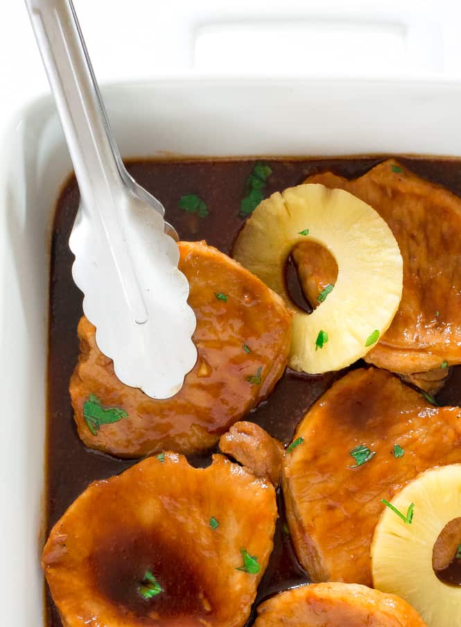 Tongs picking up a quick and easy Hawaiian Pork Chop from a baking sheet.