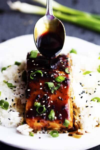 Gebakken Sesam Teriyaki Zalm op rijst met een lepel die glazuur op de zalm giet.