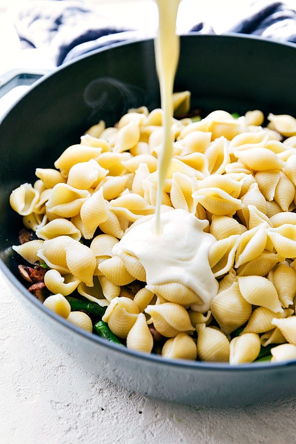 Pouring cheese sauce over the pasta in a skillet.