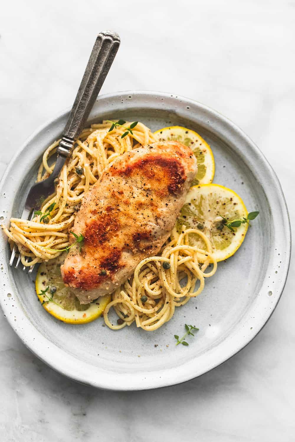 Slow Cooker Lemon Chicken Piccata on a plate with noodles and lemon slices.