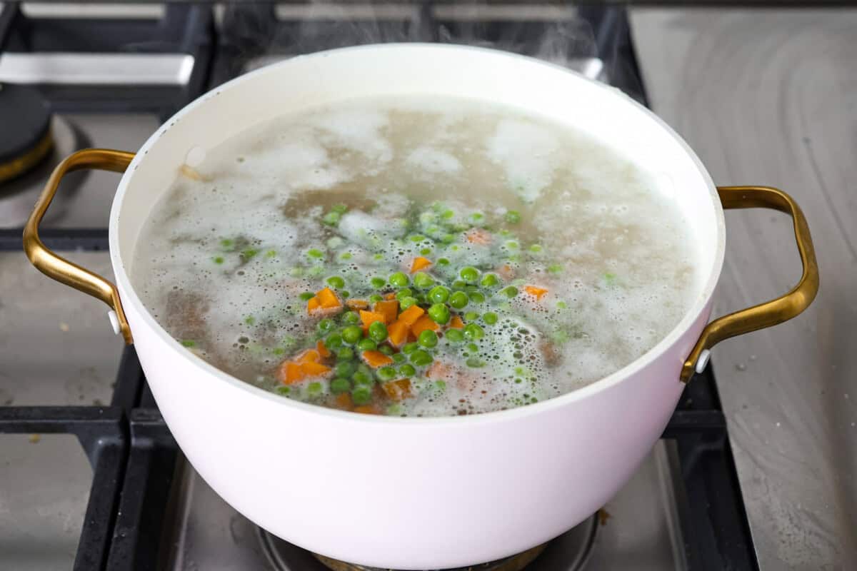 Angle shot of the noodles with peas and carrots in a pot with bowling water. 