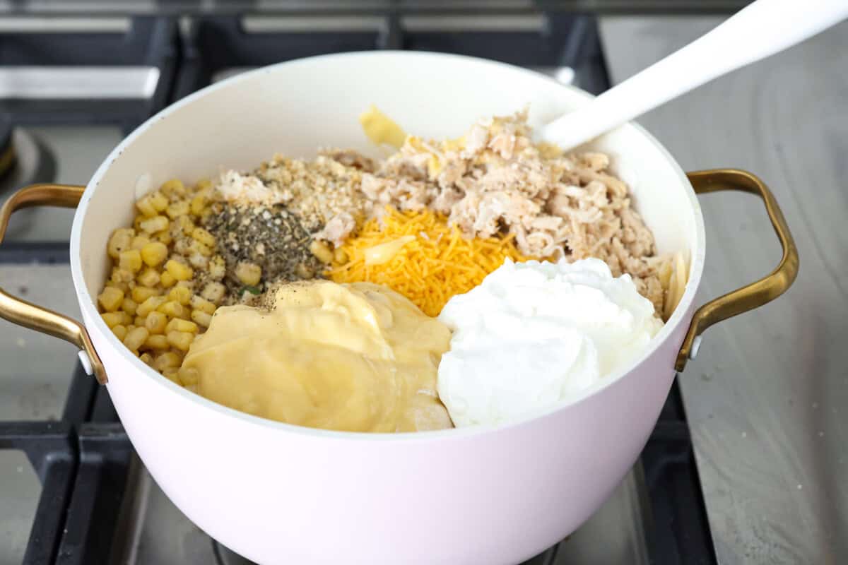 Angle shot of the cooked chicken, corn, cream of chicken soup, milk, sour cream, onion flakes, Italian seasoning, garlic powder, salt, pepper, and cheddar cheese added to the pot with the drained noodles and veggies. 