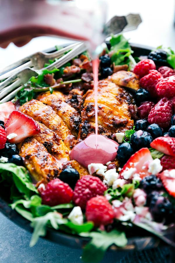 Grilled Berry Feta Chicken Salad with dressing being poured over it.