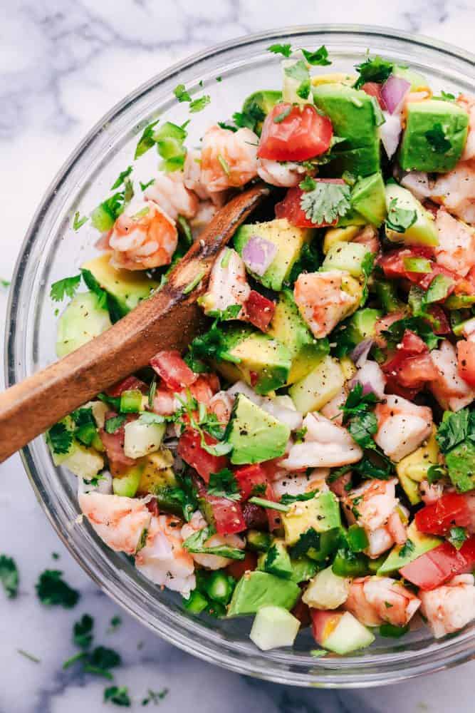 Avocado Shrimp Ceviche in a clear bowl with a wooden spoon. 