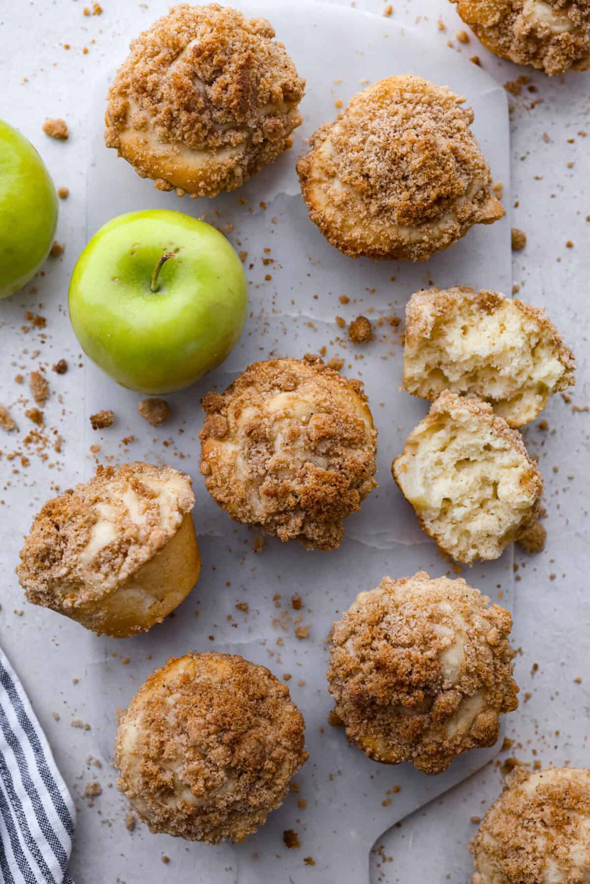 Top close view of apple crumb muffins on a marble slab with a muffin broken torn in half.