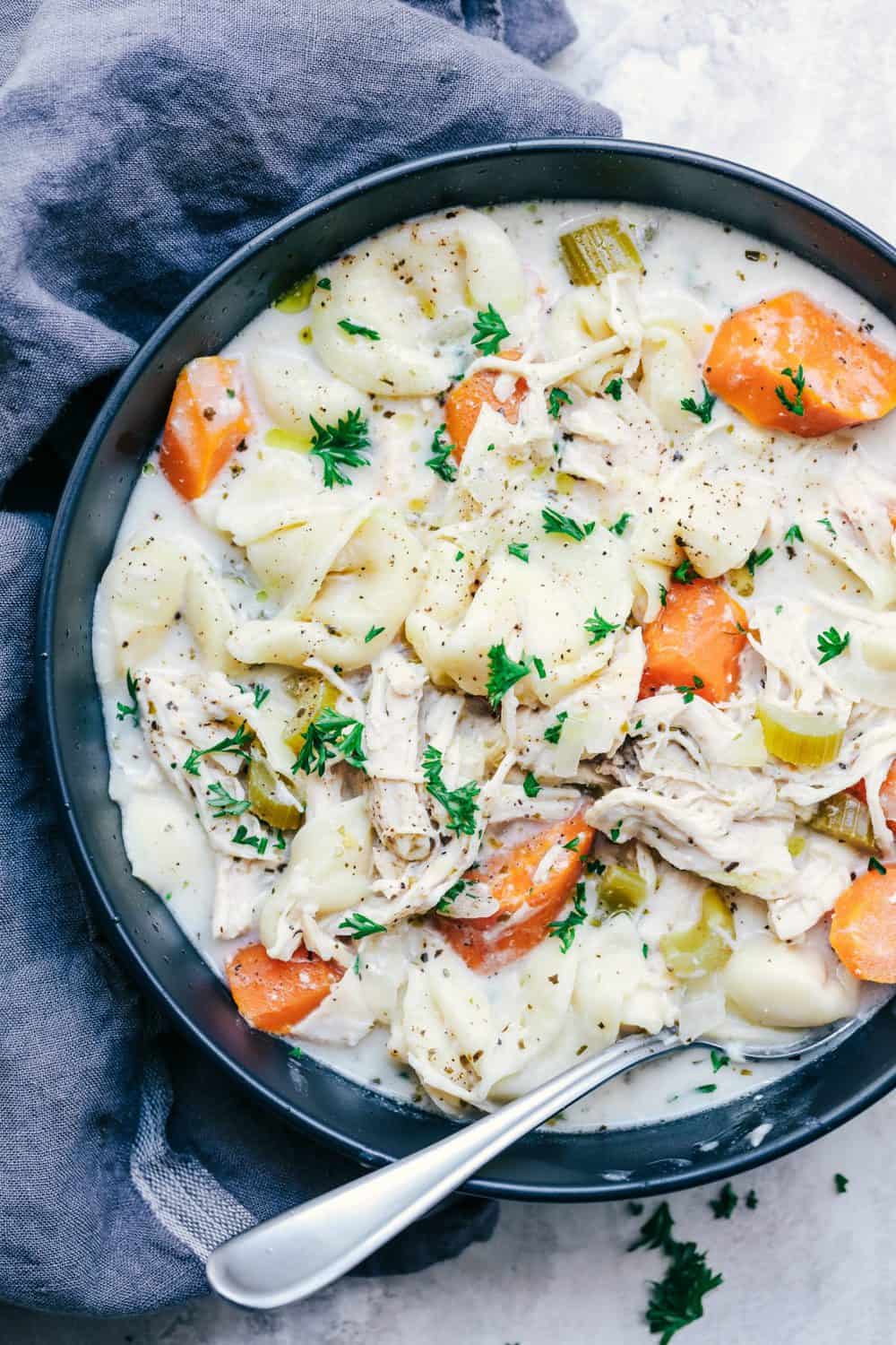 Slow Cooker Creamy Chicken Tortellini Soup in a black bowl with a spoon.