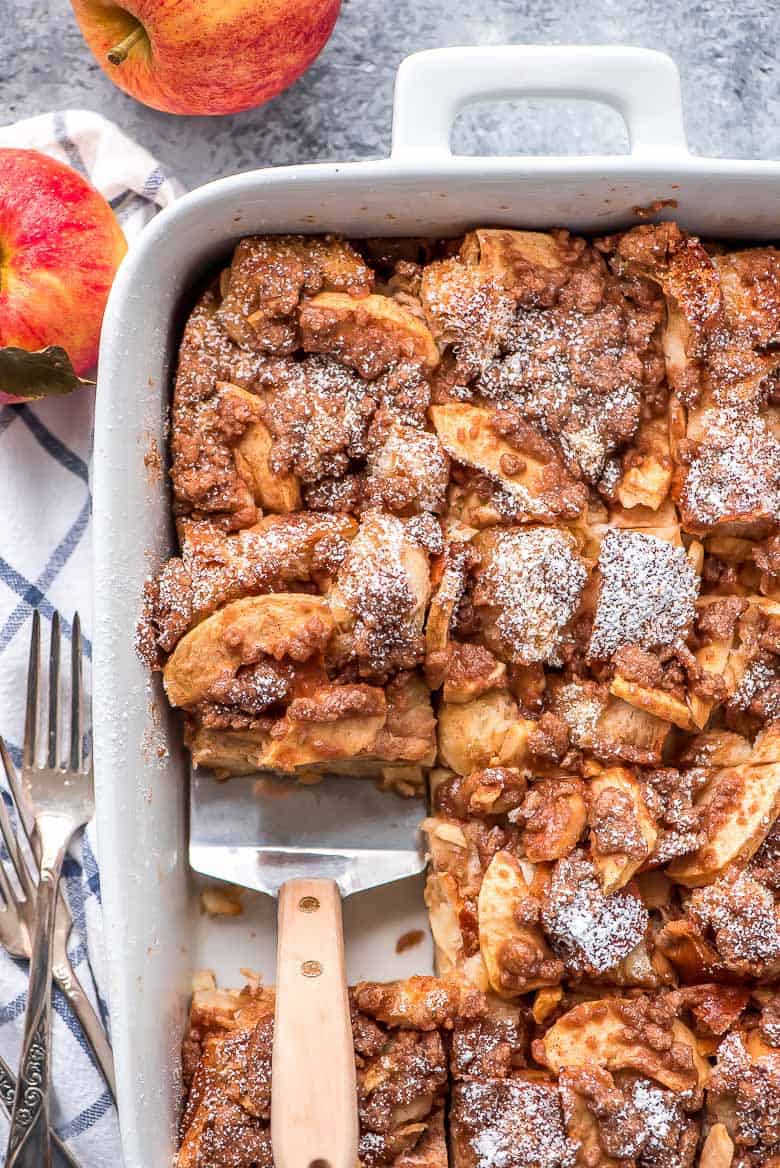 Overnight Cinnamon Apple French Toast Casserole being scooped out of a white baking dish with a spatula.