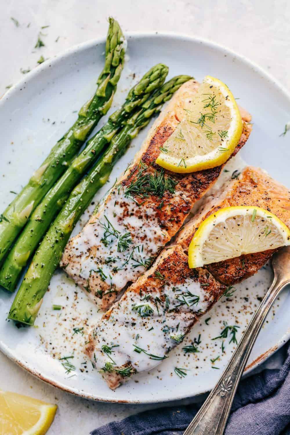 Pan Seared Salmon with a Creamy Lemon Dill Sauce on a white plate with asparagus and lemon slices.