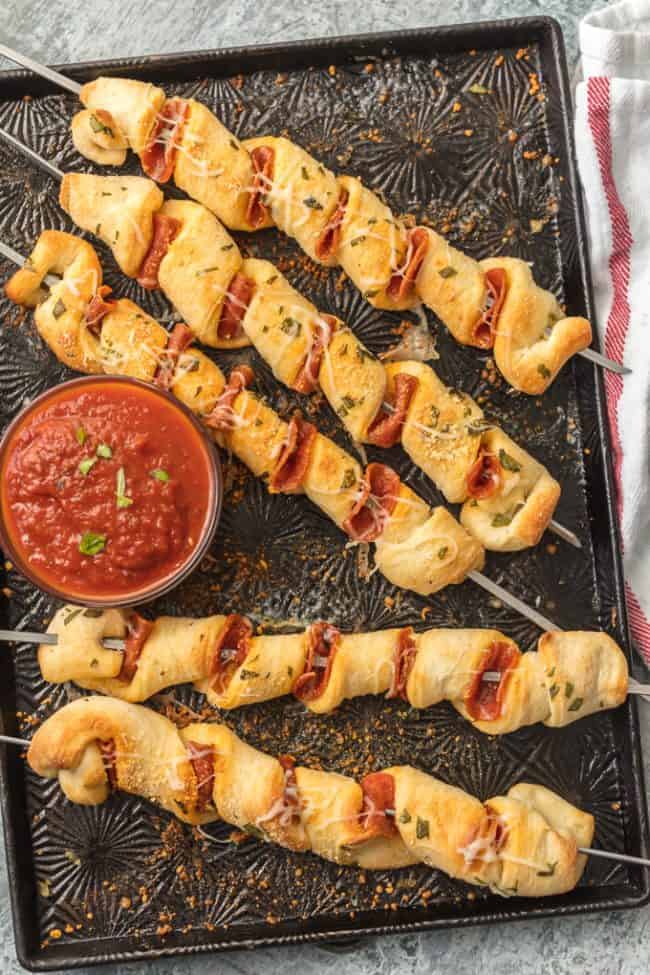 Pizza on sticks in rows with sauce.