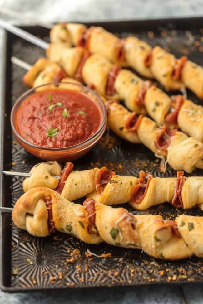 Pizza kabobs in a row with sauce.