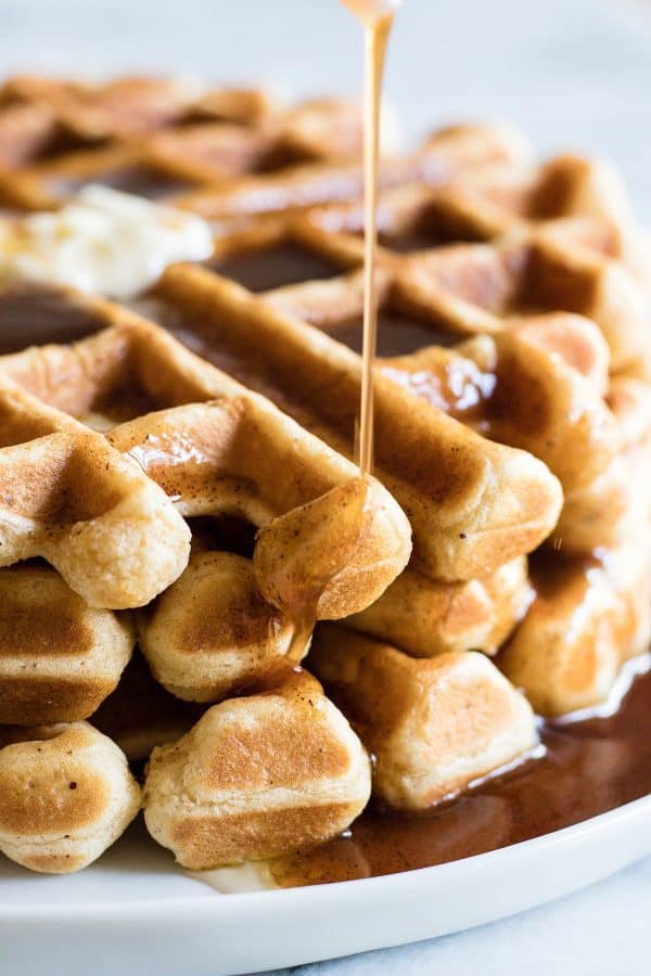 Light and fluffy waffles in a stack with syrup drizzling down on them.