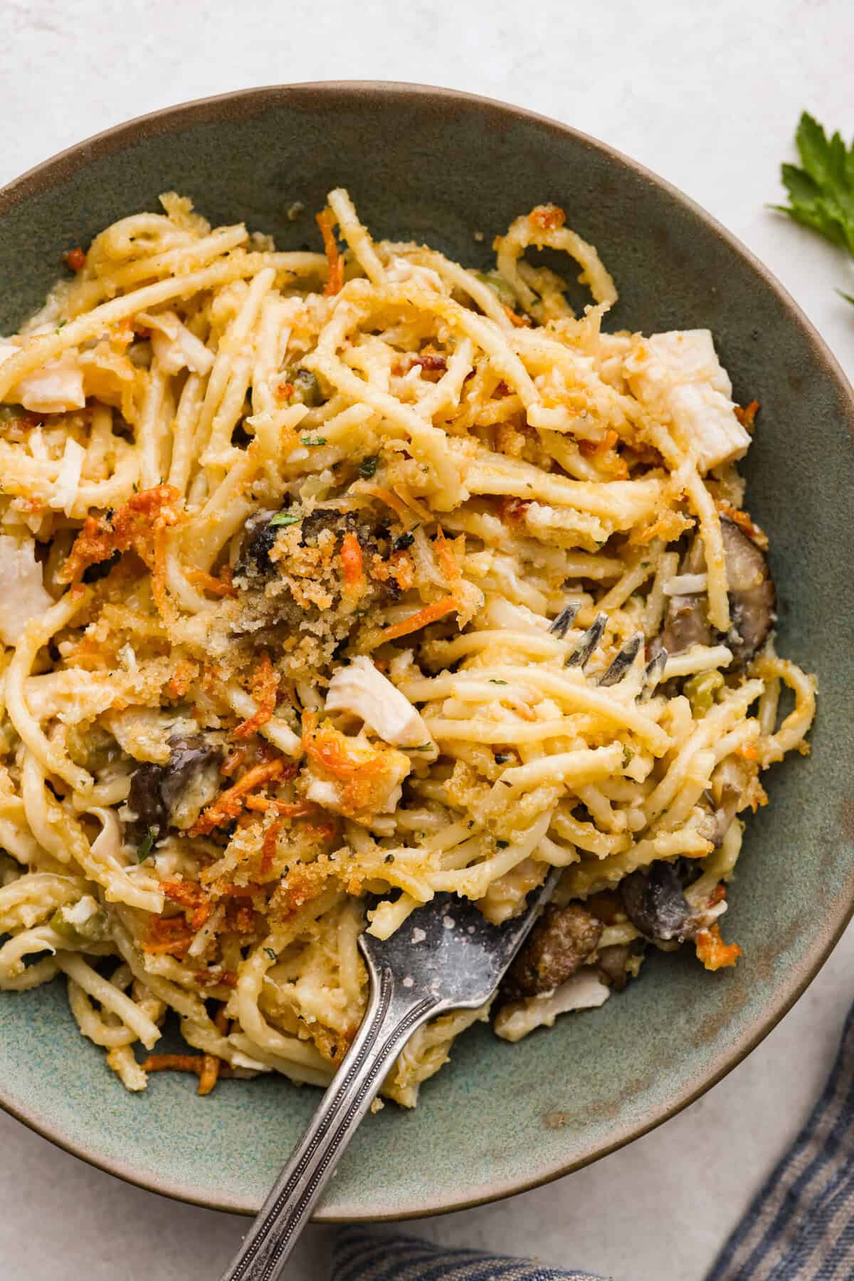 This chicken tetrazzini casserole is packed with delicious flavors and textures. It has hearty chicken, tender mushrooms, peas, and pasta, all tossed in a creamy, rich sauce. The casserole is topped with crispy, buttery breadcrumbs and a sprinkle of Parmesan cheese with the most irresistible crunch and flavor. Overhead shot of plated chicken tetrazzini.