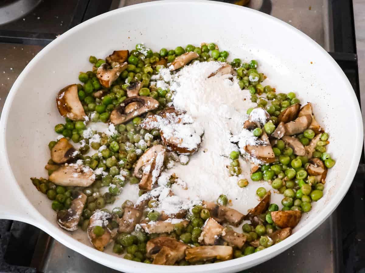 This chicken tetrazzini casserole is packed with delicious flavors and textures. It has hearty chicken, tender mushrooms, peas, and pasta, all tossed in a creamy, rich sauce. The casserole is topped with crispy, buttery breadcrumbs and a sprinkle of Parmesan cheese with the most irresistible crunch and flavor. Overhead shot of sautéed mushrooms and peas with flour on top.