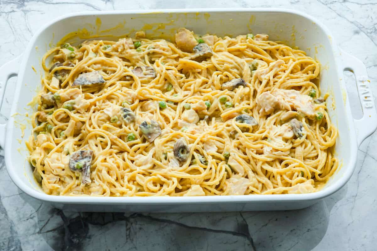 This chicken tetrazzini casserole is packed with delicious flavors and textures. It has hearty chicken, tender mushrooms, peas, and pasta, all tossed in a creamy, rich sauce. The casserole is topped with crispy, buttery breadcrumbs and a sprinkle of Parmesan cheese with the most irresistible crunch and flavor. Overhead shot of chicken and soup mixture stirred in with the pasta in the casserole dish.
