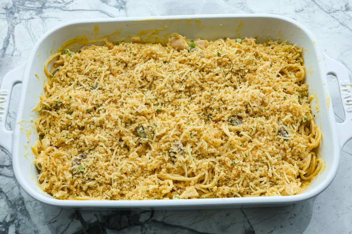 This chicken tetrazzini casserole is packed with delicious flavors and textures. It has hearty chicken, tender mushrooms, peas, and pasta, all tossed in a creamy, rich sauce. The casserole is topped with crispy, buttery breadcrumbs and a sprinkle of Parmesan cheese with the most irresistible crunch and flavor. Overhead shot of chicken tetrazzini in casserole dish before its baked.