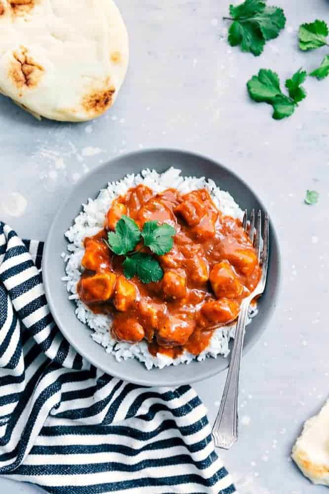 Easy Butter Chicken over white rice in a grey bowl with a fork. On the side is a pita and black and white cloth. 