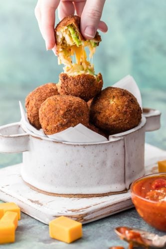 This Bacon Broccoli Cheese Arancini being pulled in half to show gooey cheese.