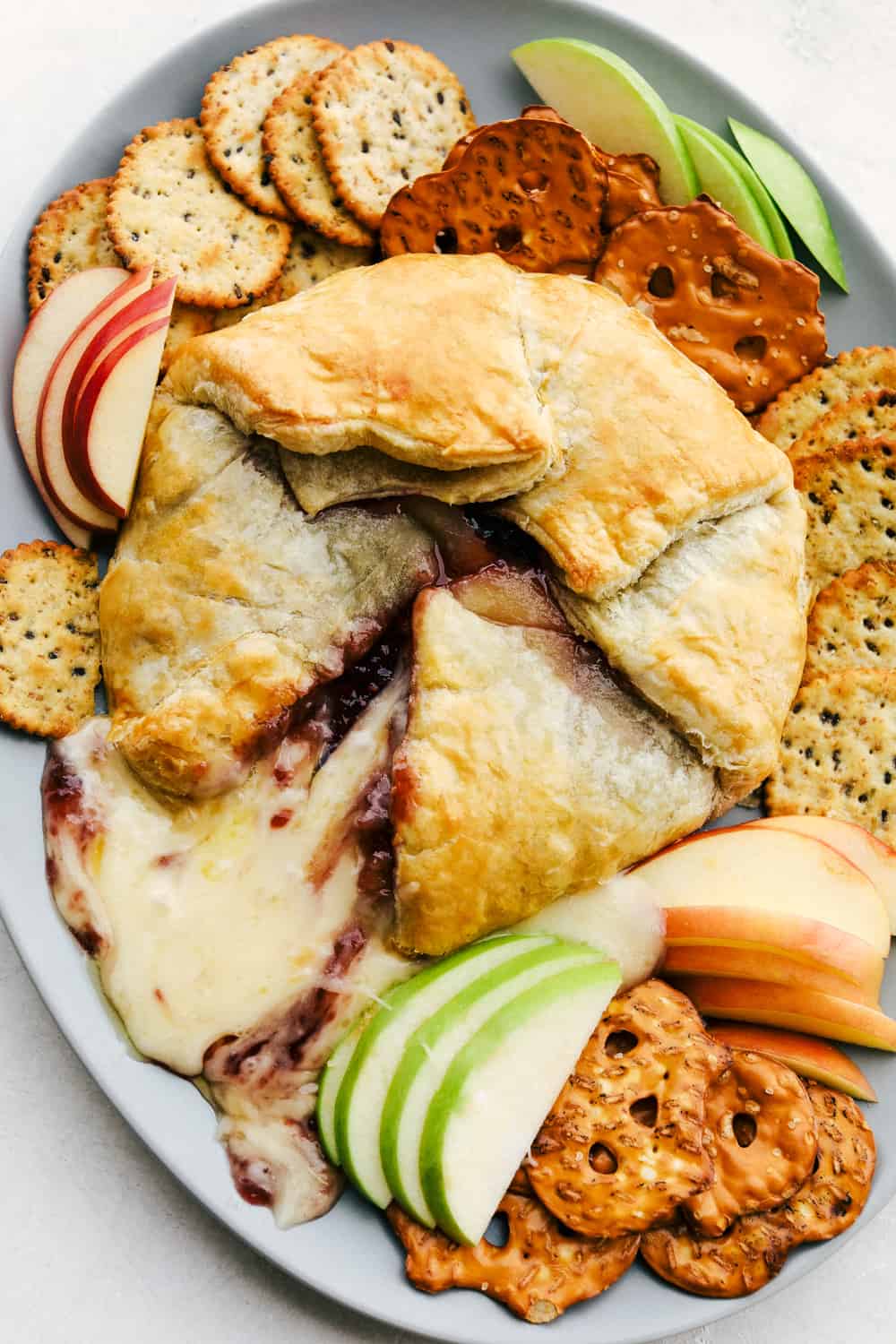 Baked Brie with Raspberries on a plant with crackers, and sliced apples.