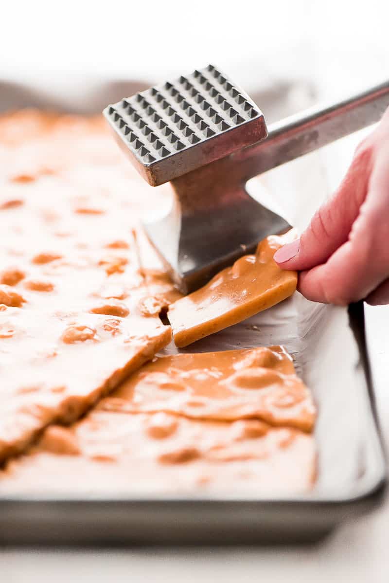 peanut brittle being broken apart with a meat tenderizer. 