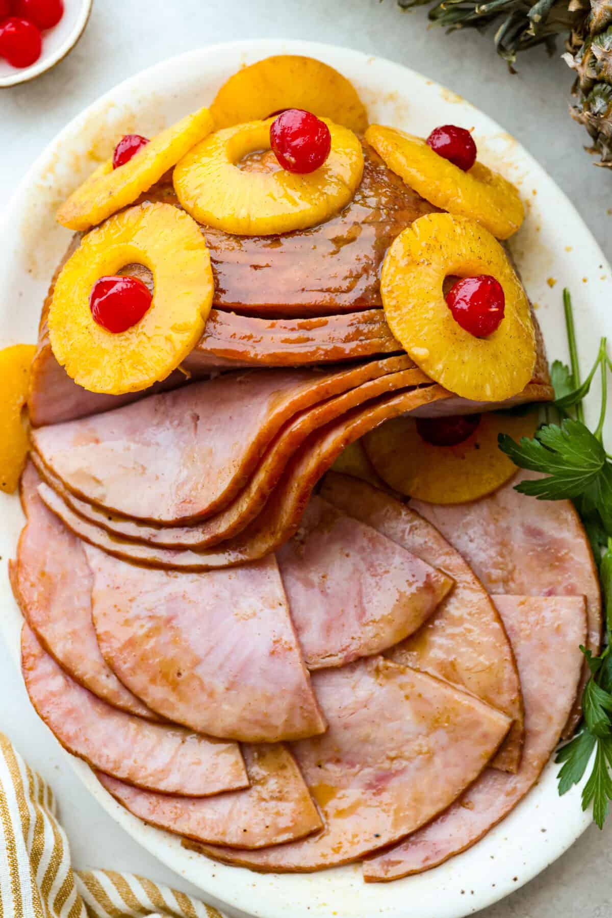 Brown Sugar Pineapple Glazed Ham is coated with a sweet and tangy spiced glaze that caramelizes on the edge of the ham. It's covered in juicy pineapple rings and maraschino cherries that add a tangy sweetness and juices to the succulent ham. Overhead shot of brown sugar pineapple glazed ham on a platter with slices cut.