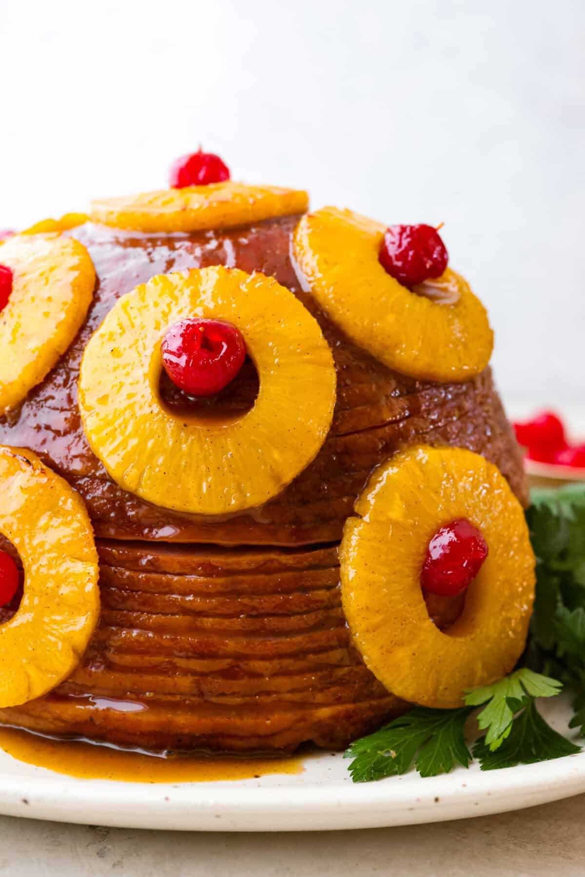 Brown Sugar Pineapple Glazed Ham is coated with a sweet and tangy spiced glaze that caramelizes on the edge of the ham. It's covered in juicy pineapple rings and maraschino cherries that add a tangy sweetness and juices to the succulent ham. Side shot of brown sugar pineapple glazed ham.