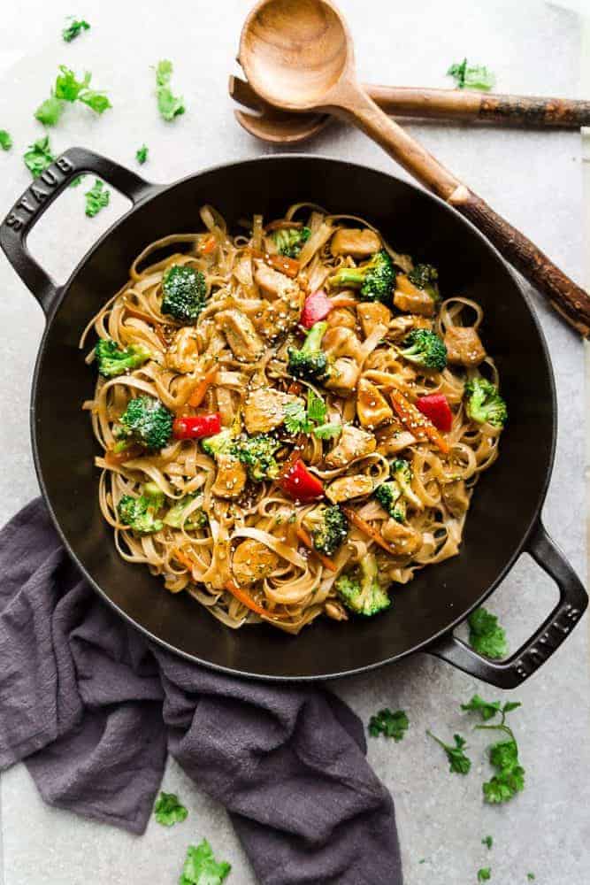 Mongolian chicken noodles in a iron skillet with wooden spoons next to it. 