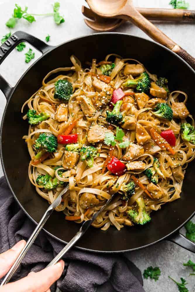 Mongolian Chicken Noodles in a iron skillet with a set of tongs and wooden spoons. 