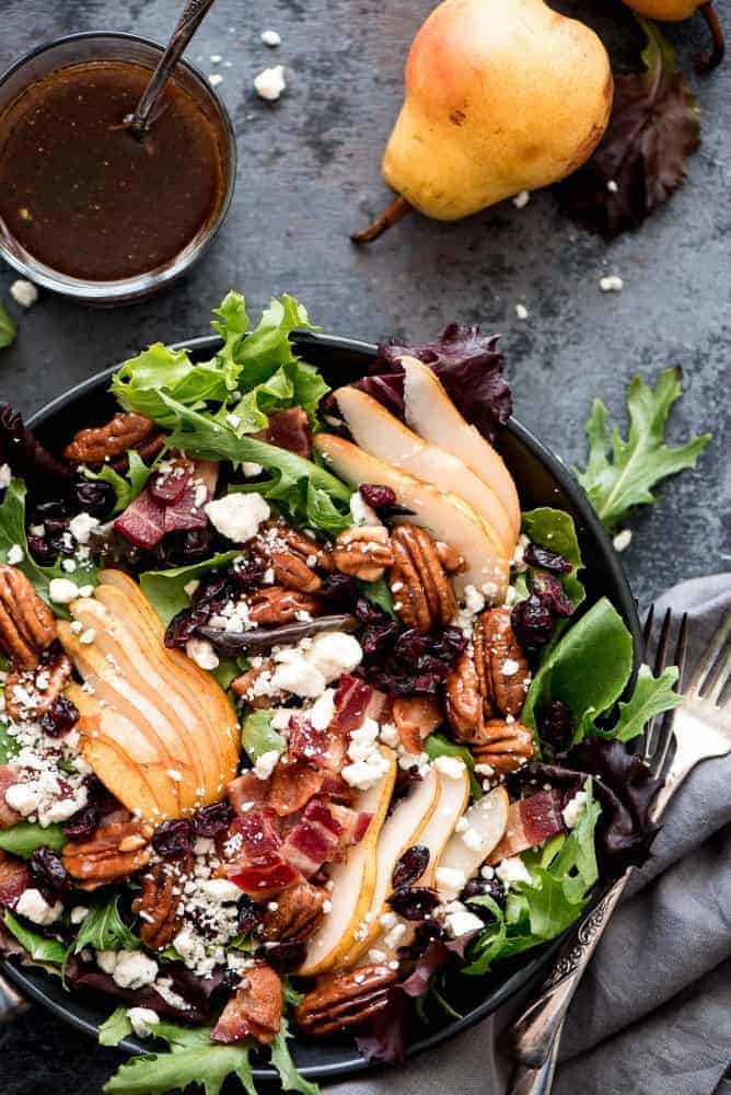 Bacon Pear Gorgonzola Salad in a black bowl with a fork, dressing, and pear on the side. 