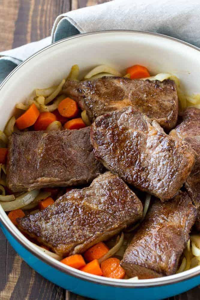 Root beer glazed short ribs with noodles and carrots in a blue iron pot.