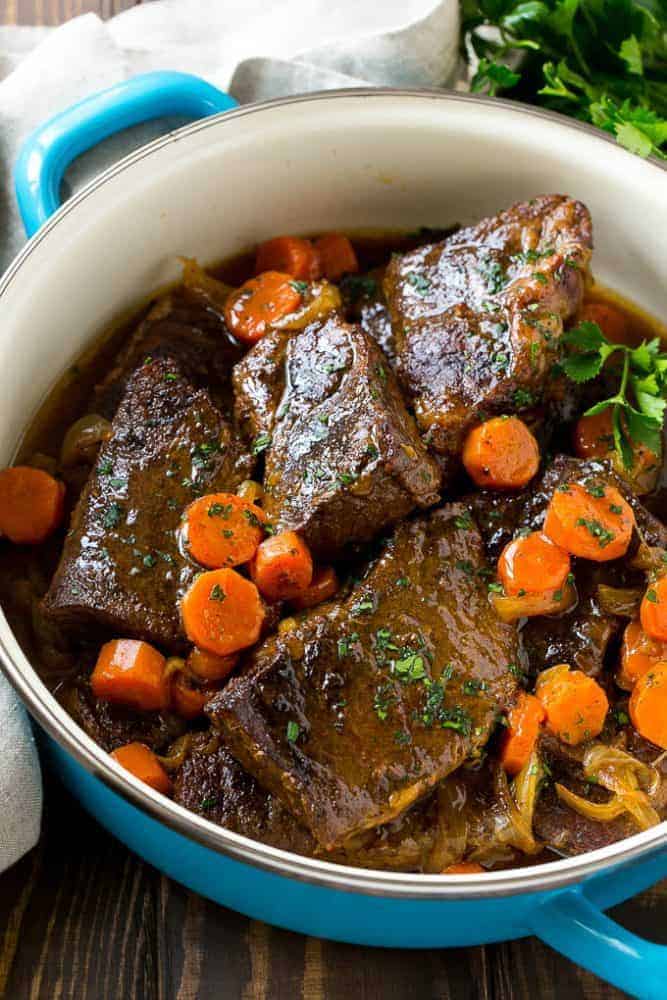 Root beer glazed short ribs with cooked carrots in a blue iron pot.