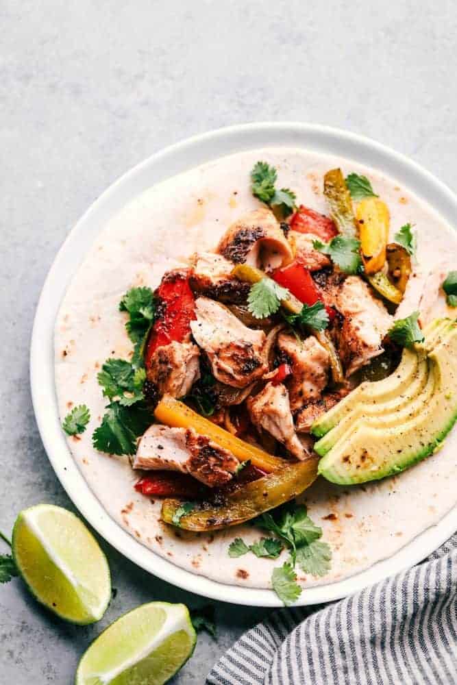 Garlic Lime Salmon Fajitas on a white plate with avocados and lime on the side. 