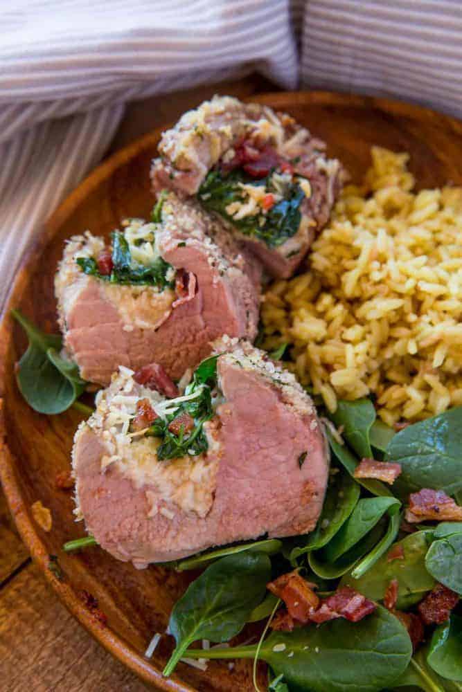Spinach and Bacon Stuffed Tenderloin with rice and spinach in a wooden bowl.