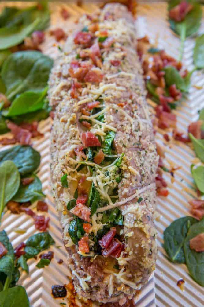 Uncooked Spinach Bacon Stuffed Pork Tenderloin on a cooking sheet.