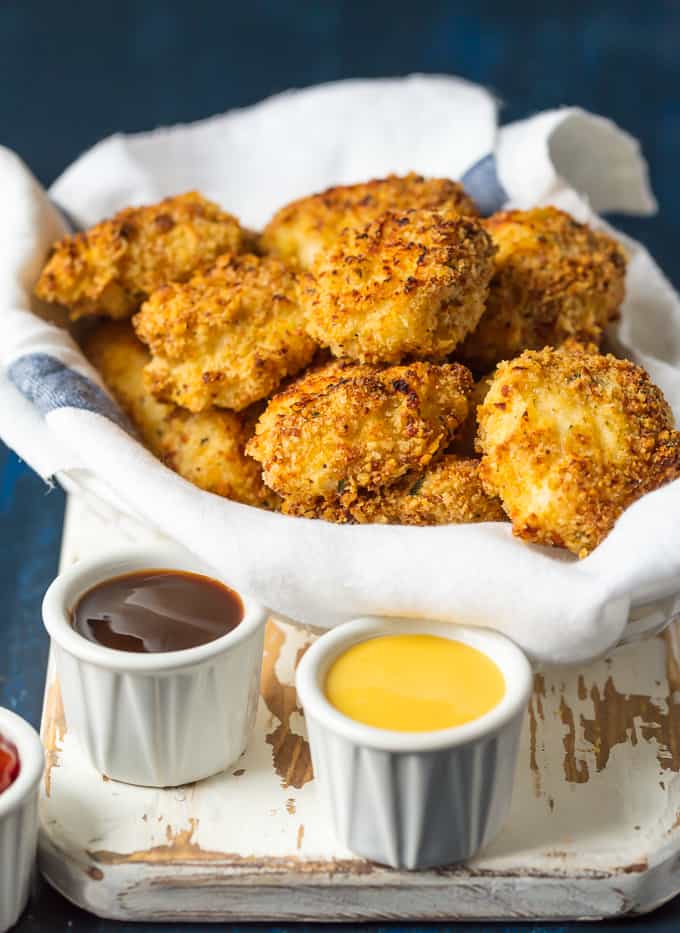 Baked Parmesan Chicken Nuggets in a bowl on a cutting board. There are three different types of dipping sauce also. 