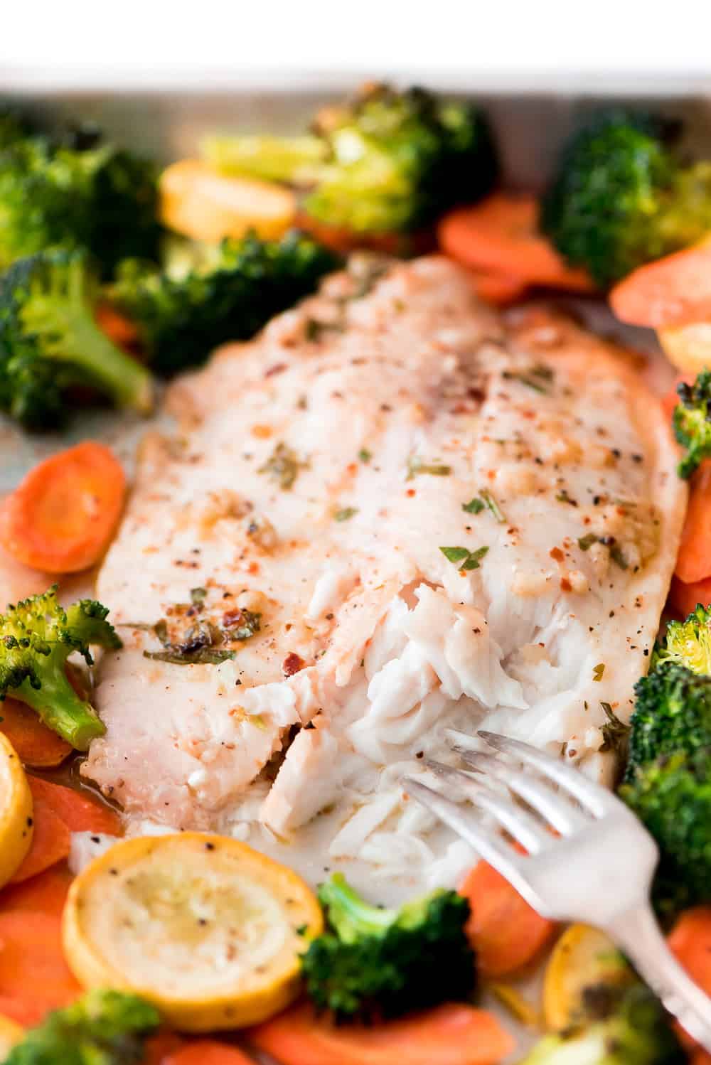 A fork pulling a bite of Baked Tilapia.