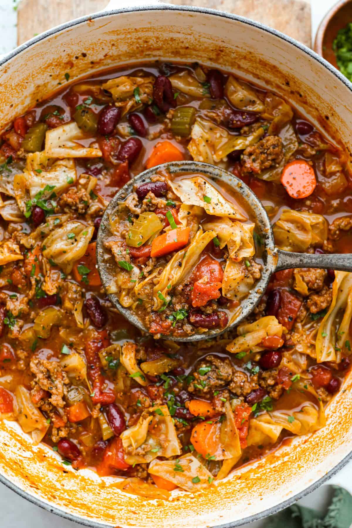 Overhead shot of beef and cabbage soup in a large pot with a ladle full of soup. 