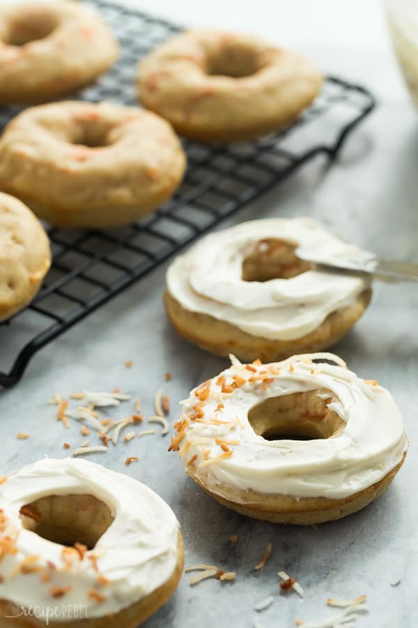 Closeup of Baked Carrot Cake Donuts with Cream Cheese Frosting. A few on a cooling rack and a few on the counter. 