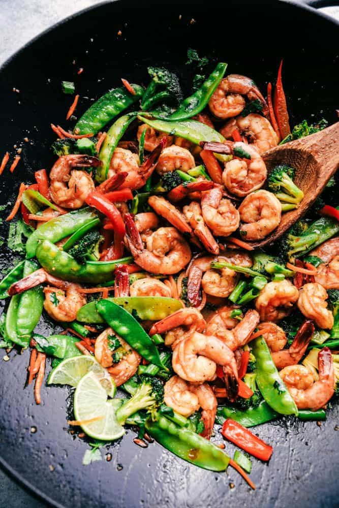 Shrimp stir fry in a wok with a wooden spoon stirring it together. 