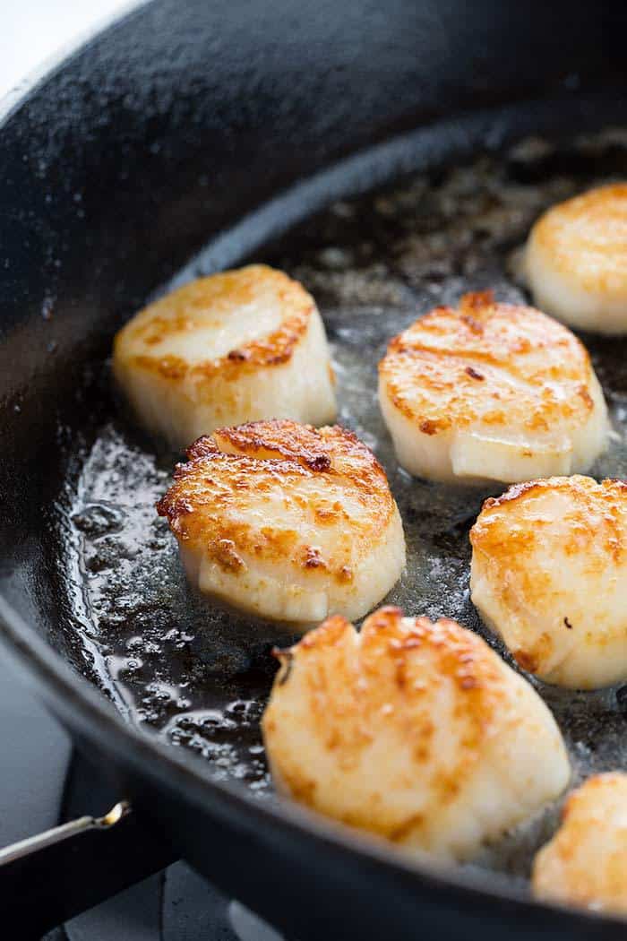 Scallops with golden crust searing in a cast iron skillet