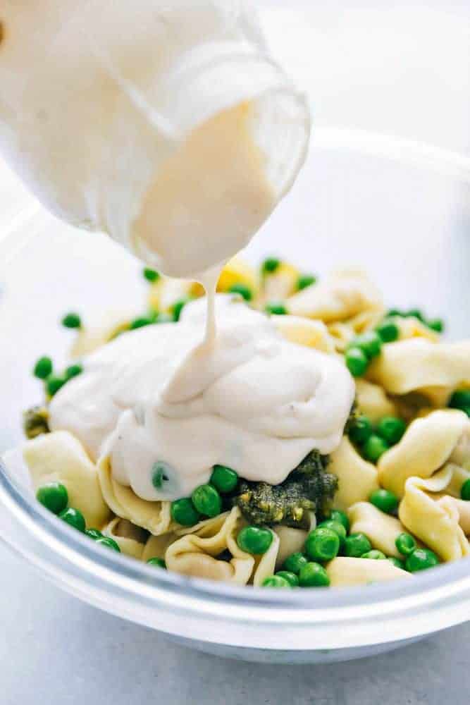 Tortellini with Sausage and peas with Alfredo sauce being poured on top. 