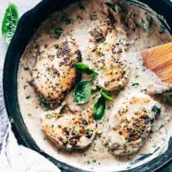 Easy creamy herb chicken in a pan with a spatula garnished with parsley and basil