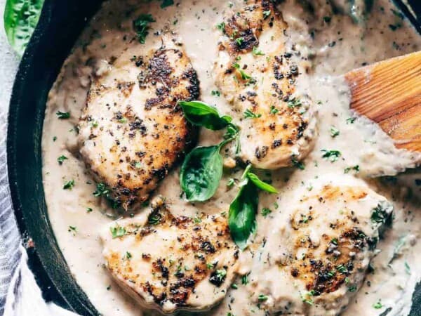 Easy creamy herb chicken in a pan with a spatula garnished with parsley and basil