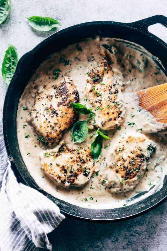Easy creamy herb chicken in a pan with a spatula garnished with parsley and basil
