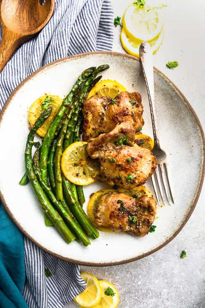 Olla instantánea de pollo con ajo y limón en un plato con espárragos y rodajas de limón.