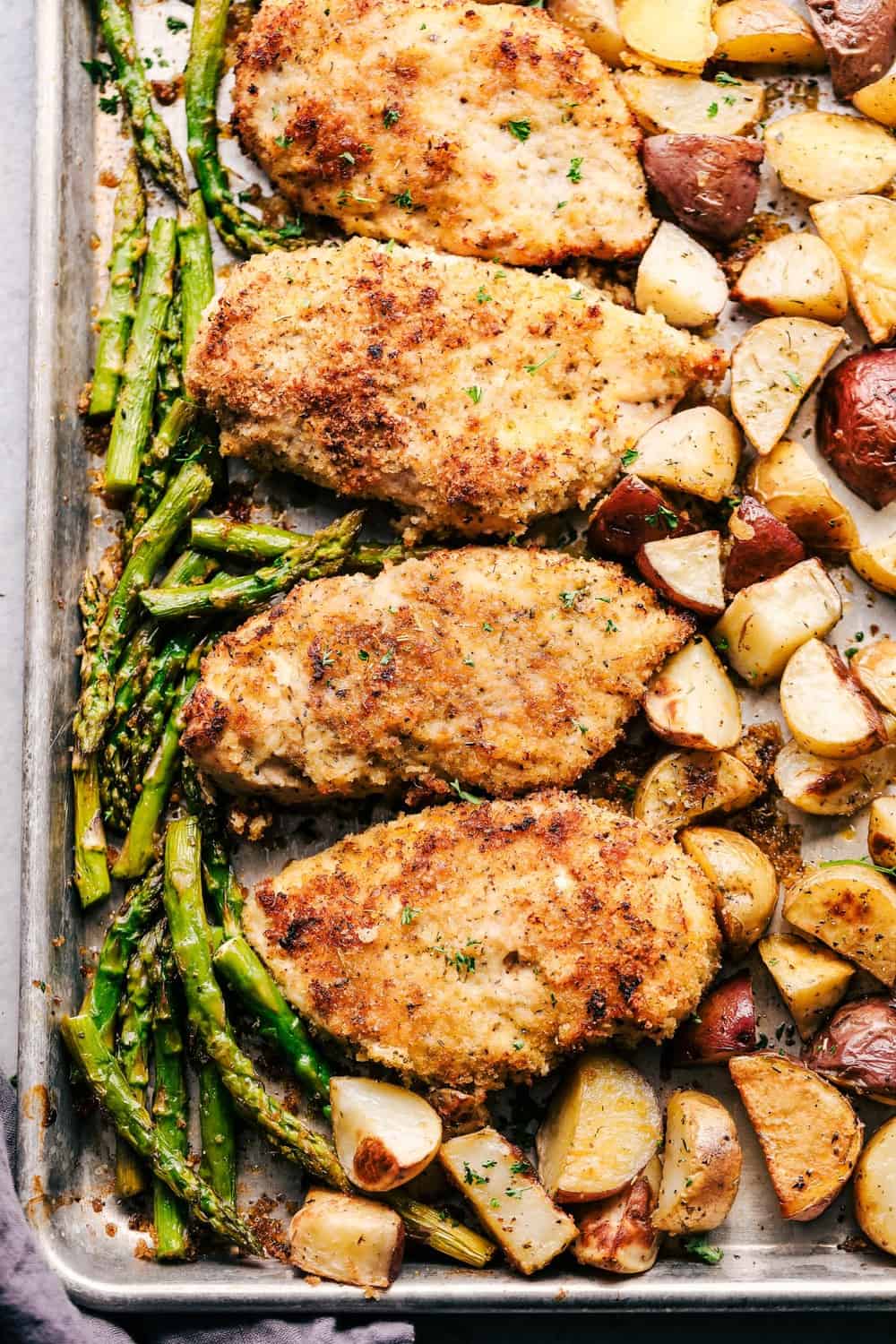 Crispy parmesan chicken on a sheet pan with potatoes and asparagus.