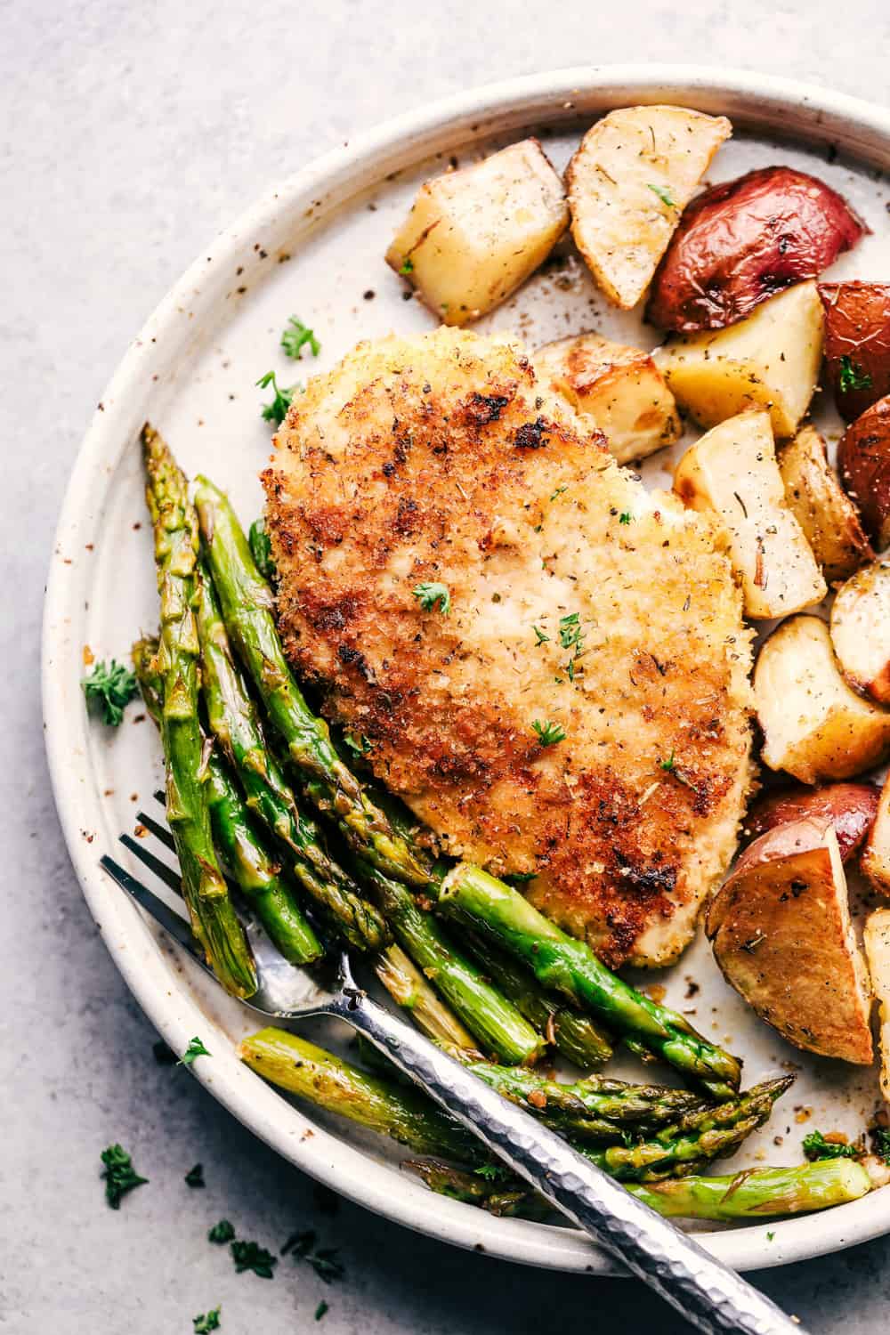 White plate with crispy parmesan chicken asparagus and potatoes.
