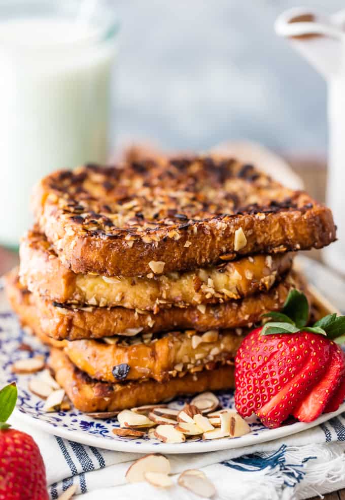 Almond French Toast with sliced strawberries on a white and blue plate. There is a glass of milk in the background. 